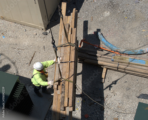 Chicago, Illinois, USA. June 28, 2022. Looking down on a construction worker who is operating a remote controled crane to move a bundle of lumber. photo