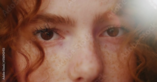 Portrait eyes sunshine young smiling woman with red curly hair look at camera. Feel happy. Summer. Outdoors at sunlight. Slow motion