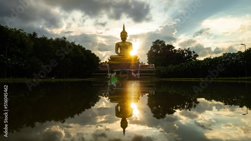 4K:Time lapse Beautiful  Big Golden Buddha statue against sunset clouds sky in Thailand temple,khueang nai District, Ubon Ratchathani province, Thailand.with Flare ,ghost and wave reflection in water.