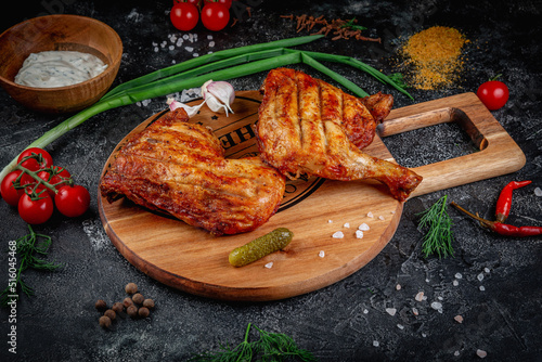 Grilled chicken legs on a dark stone table with vegetables, cream and tomato sauce. Served on a wooden board. Fast food restaurant, delivery services.