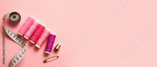 Colorful sewing threads and measuring tape on pink background with space for text