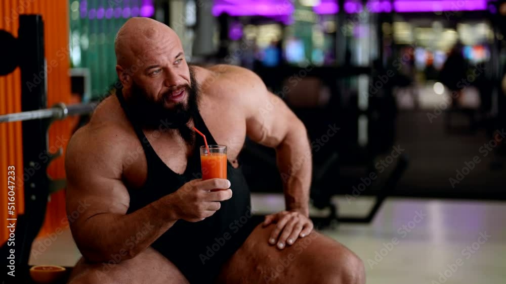 sporty man with large muscles is resting in gym and drinking vitamin