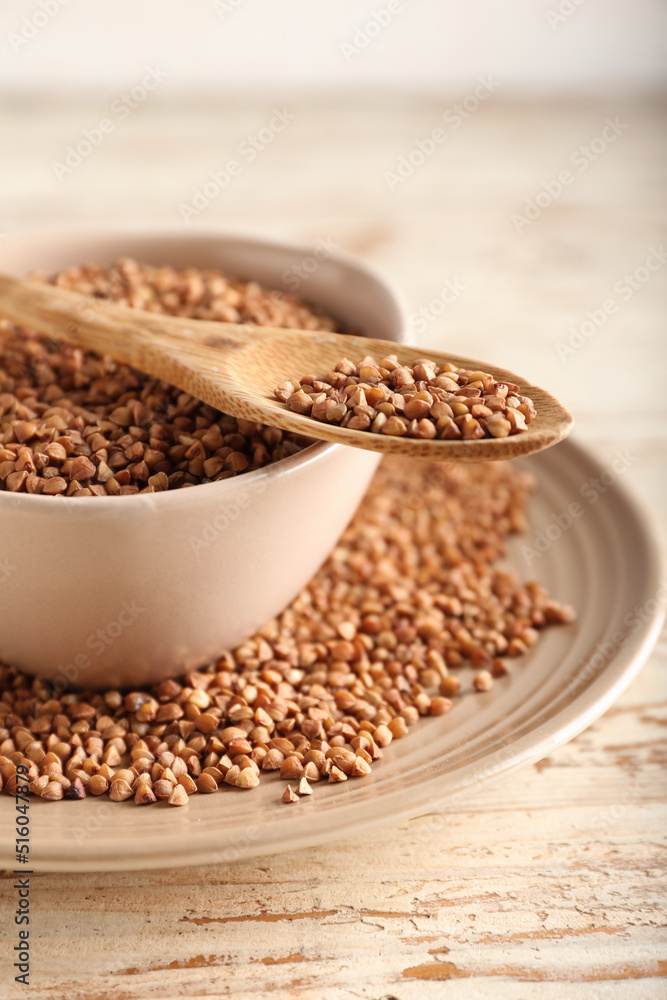 Plates and spoon with buckwheat grains on light wooden background, closeup Plates and spoon with buckwheat grains on light wooden background, closeup