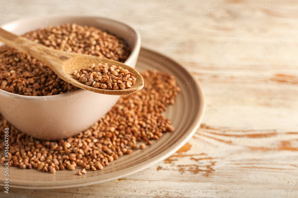 Plates and spoon with buckwheat grains on light wooden background, closeup Plates and spoon with buckwheat grains on light wooden background, closeup