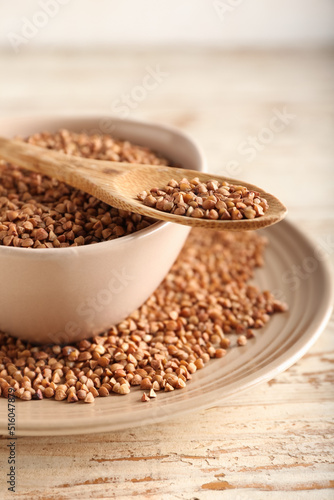 Plates and spoon with buckwheat grains on light wooden background, closeup