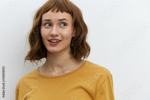 a beautiful, sweet, relaxed woman stands on a light background in a yellow T-shirt and looks away with a pleasant smile. Horizontal photo with an empty space for inserting an advertising layout © Tatiana