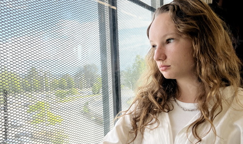 European girl with blond long hair in a white shirt rides in a skytrain she sadly looks out the window she is sad waiting for her A long road outside the window flashes into nature Vancouver Surrey