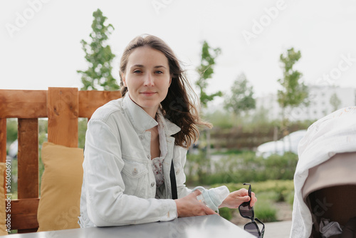 A woman with long hair is sitting near the baby stroller in the cafe. A lady in a white dress is posing near the stroller.