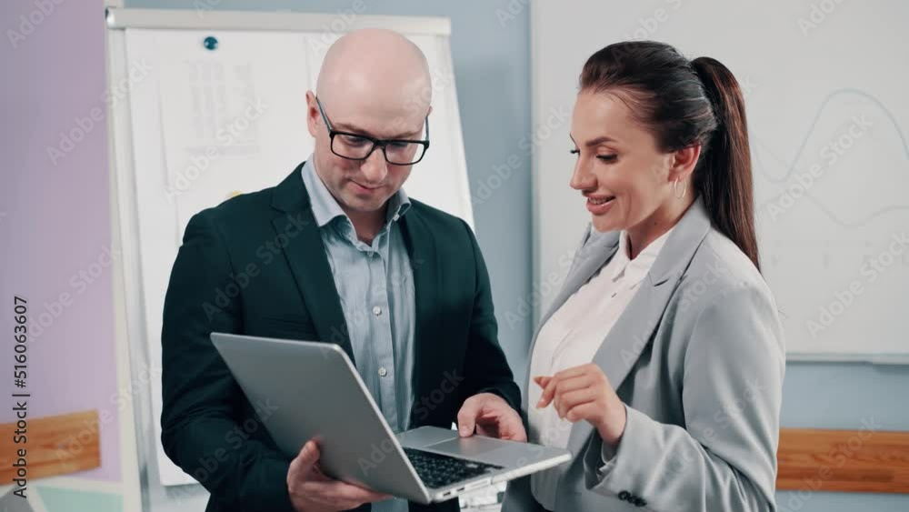 Couple of office workers discussing business. Young man and woman are looking at a laptop screen and talking. Couple of office workers discussing business. Young man and woman are looking at a laptop screen and talking.