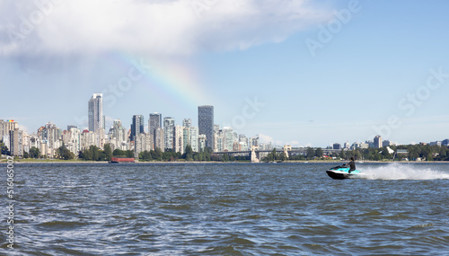 Adventurous Caucasian Woman on Water Scooter riding in the Ocean. Modern City in background. Downtown Vancouver, British Columbia, Canada. Colorful Rainbow © edb3_16