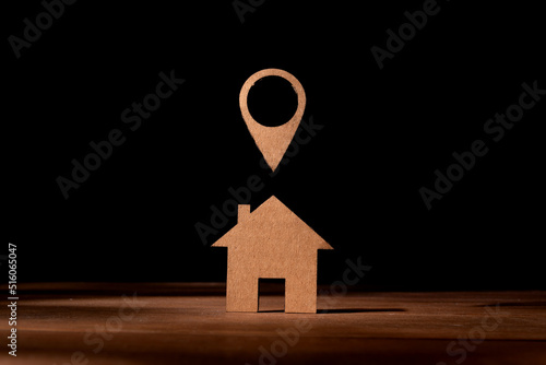 Cardboard cut-out representation of a little house with the position symbol on the map. Concept of having as a destination the acquisition of a house