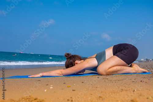 A beautiful girl is doing yoga on the beach near the sea
