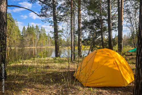 A yellow tent on the bank of a forest river.