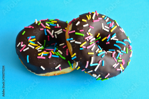 two chocolate donuts with pink, yellow, blue and green sprinkles isolated on blue background