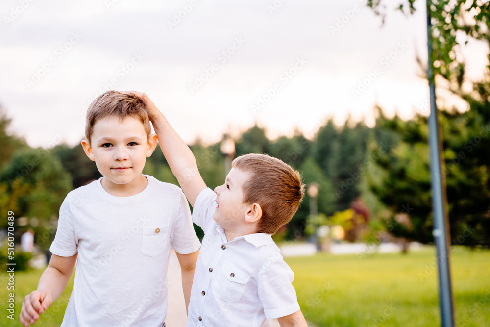 Fototapeta premium A little boy measures his older brother's height with his hand in a park in nature. Children play together.