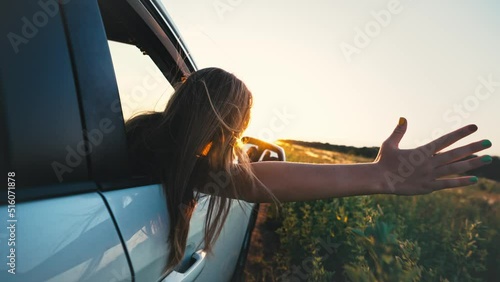 Happy family travel. Little girl leaning out of car window waving hand. Happy child girl putting her arm out of open window of a car. Summer road trip concept. photo