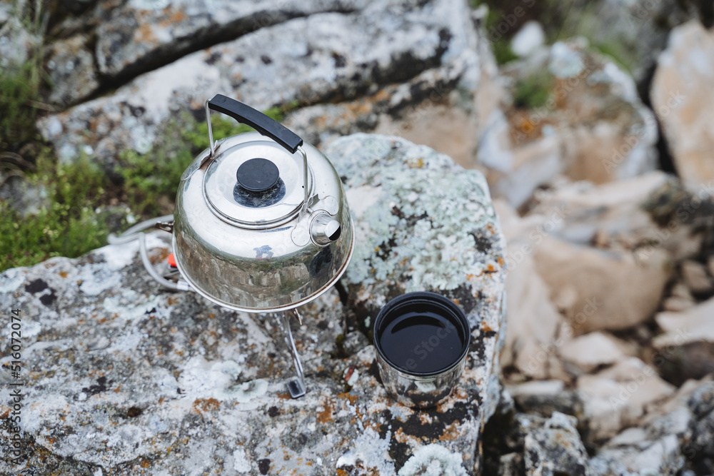 Drink tea in nature in the mountains, a tin kettle stands on a stone tea poured into a mug, breakfast in the mountains, boil water, brew a hot drink, lunch on a hike. Drink tea in nature in the mountains, a tin kettle stands on a stone tea poured into a mug, breakfast in the mountains, boil water, brew a hot drink, lunch on a hike.