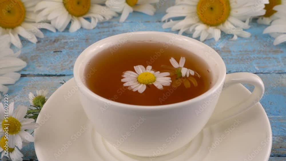 Composition with chamomile flowers and white cup of herbal tea on vintage light blue wooden table top. Summer theme. Composition with chamomile flowers and white cup of herbal tea on vintage light blue wooden table top. Summer theme.