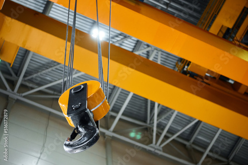 Hook assembly of yellow crane hangs under ceiling in shop