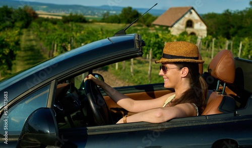 Happy woman enjoying summer vacation, driving by cabriolet car, smiling, having fun, wearing straw hat.