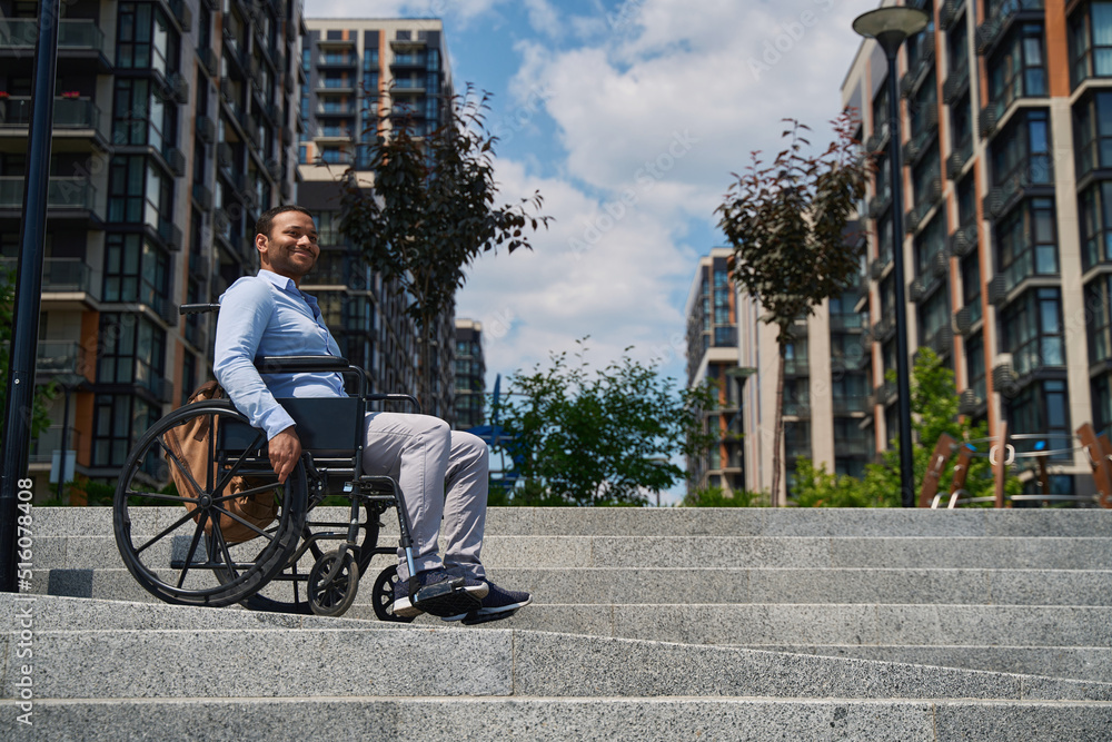 Joyous wheelchair-bound male person descending stairs outdoors