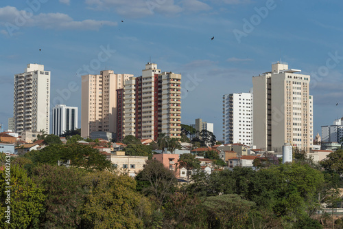 Urban landscape shows the neighborhood with single storey houses, buildings, treetops and blue sky, Piracicaba SP Brazil.