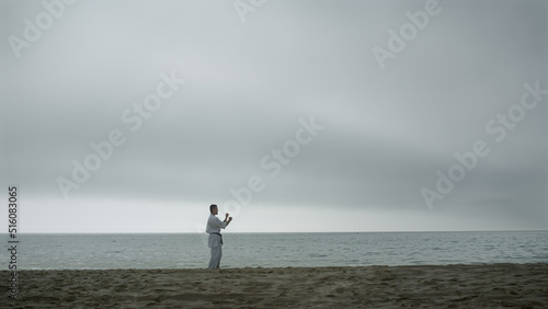 Fighter training martial arts on beach. Karate man practicing combat technique