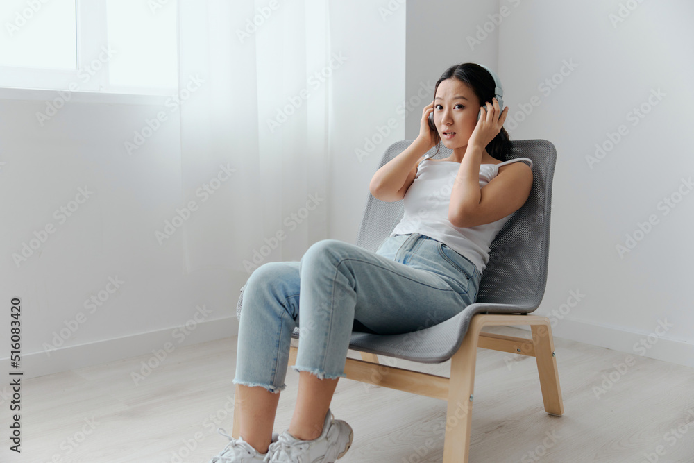 Excited shocked tanned lovely young Asian woman in headphones listens to external sounds look aside at home interior living room. Sound Studio Stream Social media concept. Cool offer Banner Wide angle