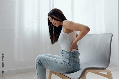 Suffering from scoliosis osteochondrosis after long study pretty young Asian woman feel hurt joint back pain laptop in incorrect posture sit on chair. Injuries Poor health Illness concept. Cool offer