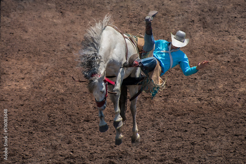 Fotografie A Rodeo cowboy is falling off on the left side of a bucking bronco