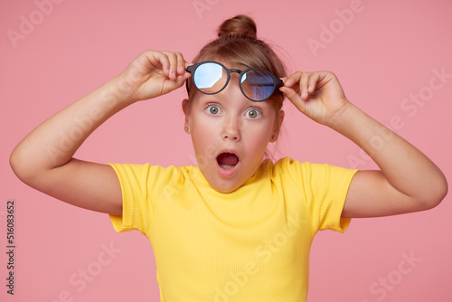 Smart child girl in yellow clothes with eyeglasses on a pink background shows thumbs up. Children's education concept