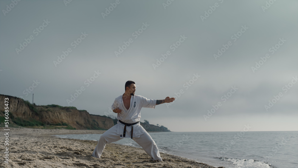 Karate athlete practicing kicks on sunny beach. Sporty man training martial arts Karate athlete practicing kicks on sunny beach. Sporty man training martial arts