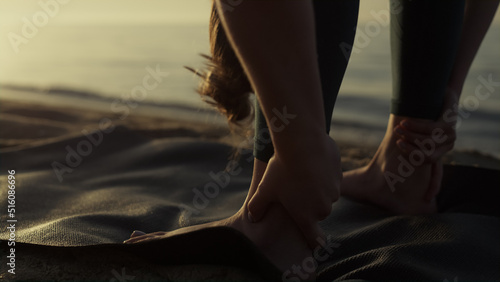 Flexible sportswoman bending body to feet on beach closeup. Yoga woman training 