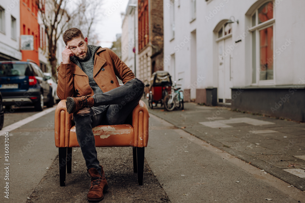 Obraz premium confused man in thoughts sit on old grungy chair in the middle of a street of a winter cold city and look while being in emotional feeling and think about problems, past, future and new ideas