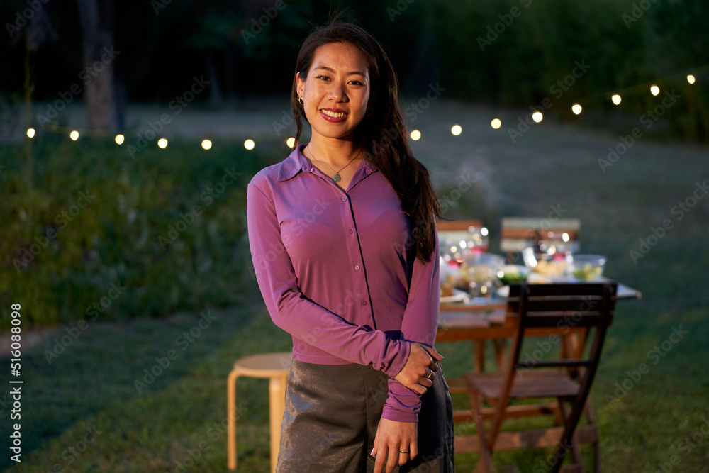 Portrait of an asian waitress looking at the camera. Chinese female restaurant worker with a nice smile is standing on the terrace in front of a table.