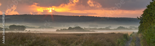 Landscape view of fog over remote field with copy space at sunset. Mist covering a vast expanse of countryside meadow in Germany at dawn. Smoke from wildfire or bush fires rolling over nature reserve