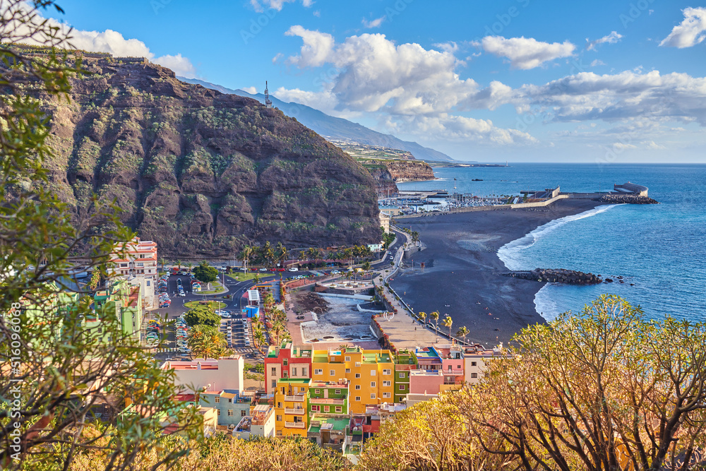 Beautiful ocean coastline with black beach sand on Puerto de Tazacorte. Colorful town houses or tourism holiday resort accommodation near a mountain and seaside in La Palma, Spain
