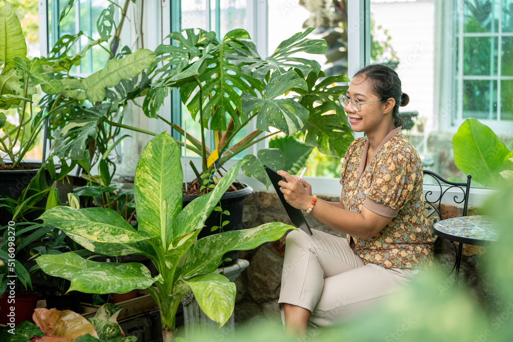 Obraz premium Young woman working with Tablet Laptop at Green house Garden Shop, Digital Nomad woman Remote working Online job or Teaching online Lifestlye Digital Nomad, Woman Freelance working freedom