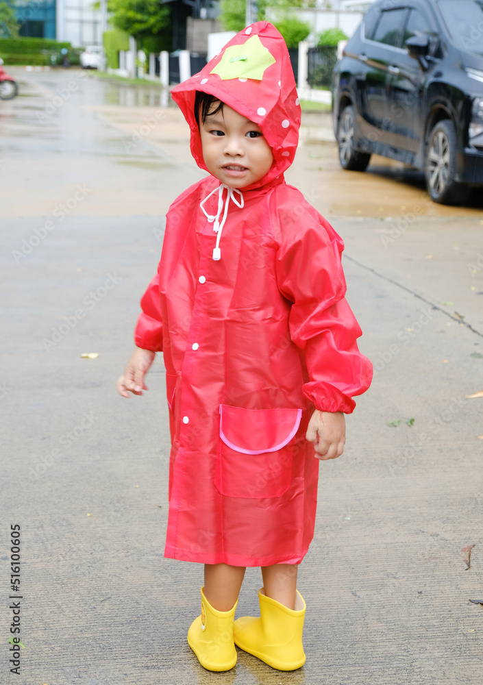 A boy wearing a red raincoat in public park having fun to playing with the rain.