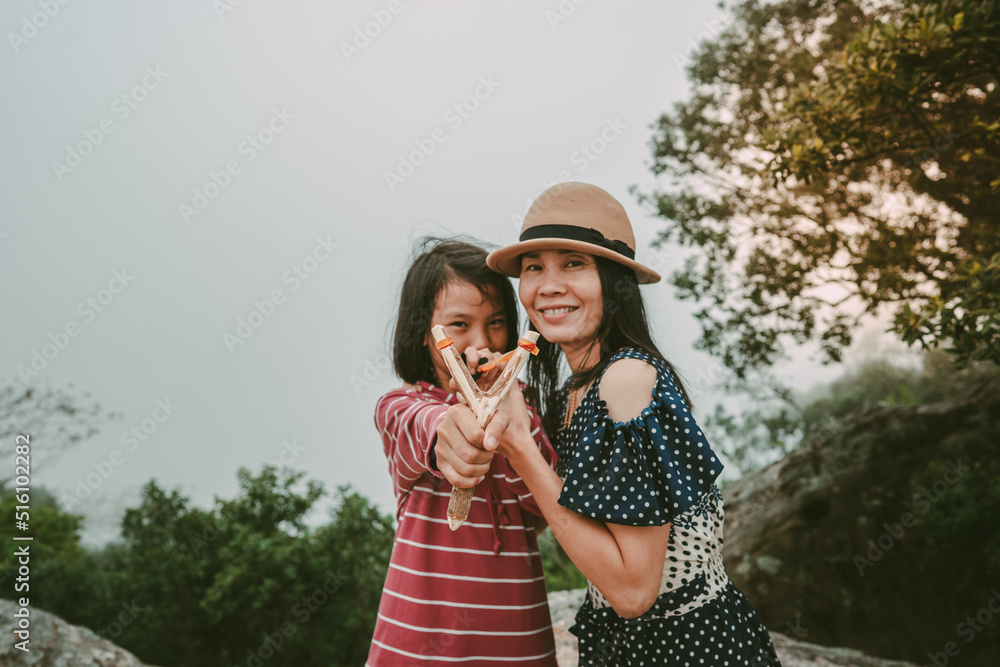 Children and mother holding slingshot for shooting seed of plants to forest on foggy and sky morning background Children and mother holding slingshot for shooting seed of plants to forest on foggy and sky morning background