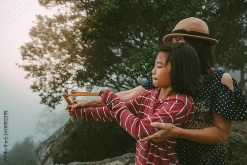 Children and mother holding slingshot for shooting seed of plants to forest on foggy and sky morning background 