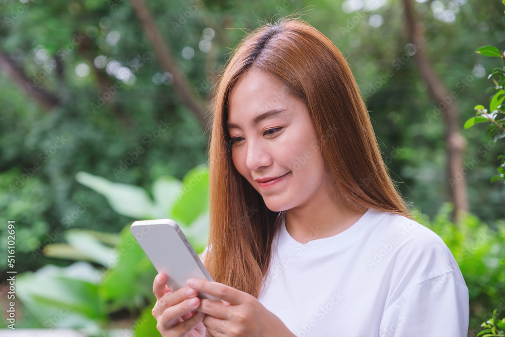 Portrait image of a beautiful young asian woman holding and using mobile phone in the outdoors Portrait image of a beautiful young asian woman holding and using mobile phone in the outdoors