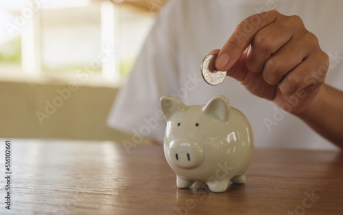 Closeup image of a woman putting coin into piggy bank for saving money concept