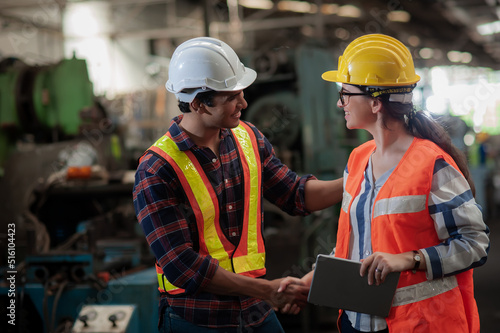 A smiling female engineer shakes hands to greet a tall, handsome, dark-skinned engineer wearing workwear safety uniform while working in an industrial factory.Teamwork and gender diversity concept.