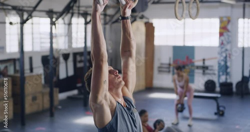Fit man using gymnastic rings for pull ups for training exercise in a gym. Strong, athletic trainer with chalk hands working on upper body strength in a HIIT fitness class. Focused on muscle growth