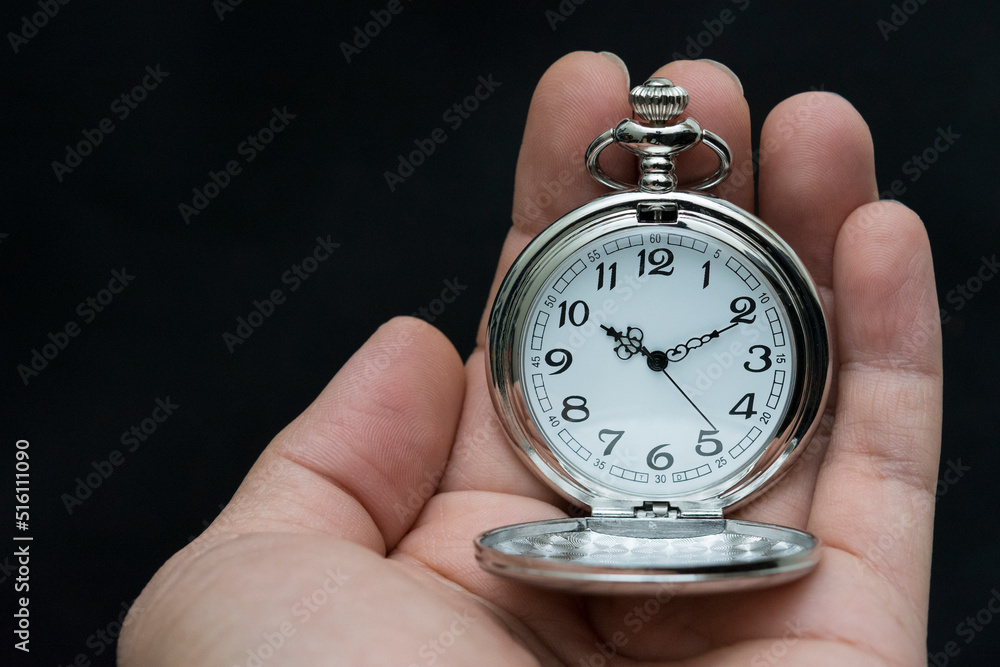 Male hand holding antique pocket watch. Isolated on black background.