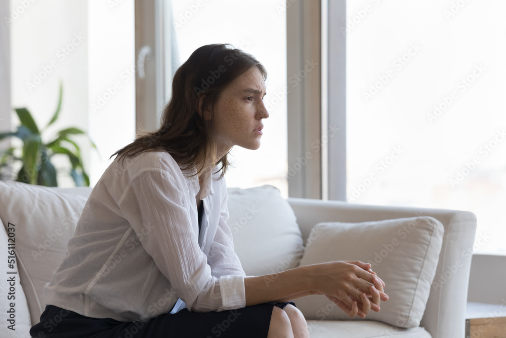 Sad disappointed freckled woman sits on sofa at home alone staring into distance thinking over split in relationships or problems, personal failure. Break up, unrequited love, life troubles concept Sad disappointed freckled woman sits on sofa at home alone staring into distance thinking over split in relationships or problems, personal failure. Break up, unrequited love, life troubles concept