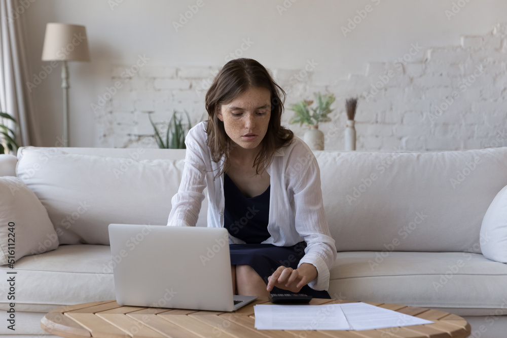 Young woman busy in household expenses calculations, check expenditures using calculator, paying bills, taxes on-line on computer. E-bank app, finances, personal budget control and management concept Young woman busy in household expenses calculations, check expenditures using calculator, paying bills, taxes on-line on computer. E-bank app, finances, personal budget control and management concept