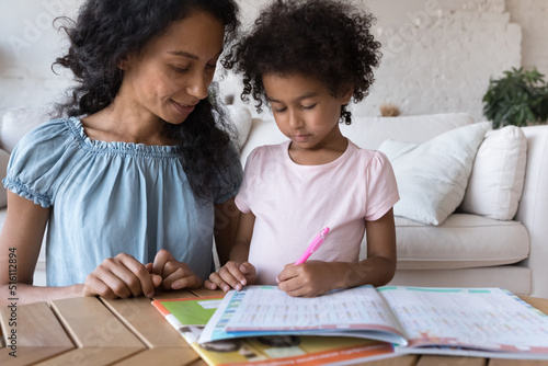 African mom help to cute little daughter with homework at home, preschool girl preparing for school do exercises, math tasks looks focused, close up. Studying, tutoring, education, development concept