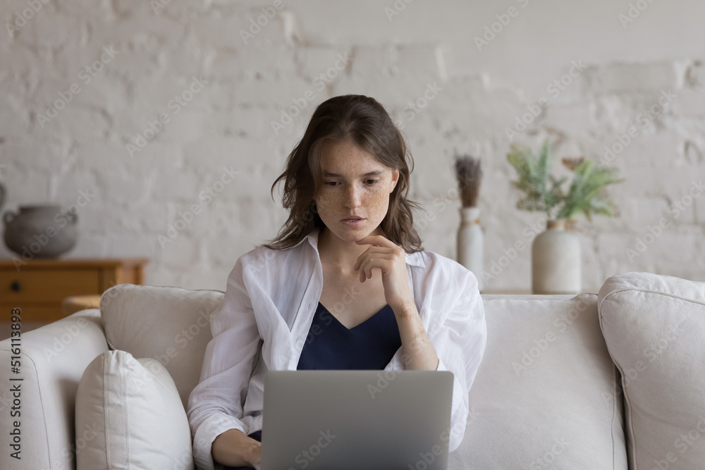 Attractive pensive young freckled woman sit on couch studying or working on-line use laptop. Freelance, e-learn, young generation and modern wireless tech, internet connection usage, education concept Attractive pensive young freckled woman sit on couch studying or working on-line use laptop. Freelance, e-learn, young generation and modern wireless tech, internet connection usage, education concept